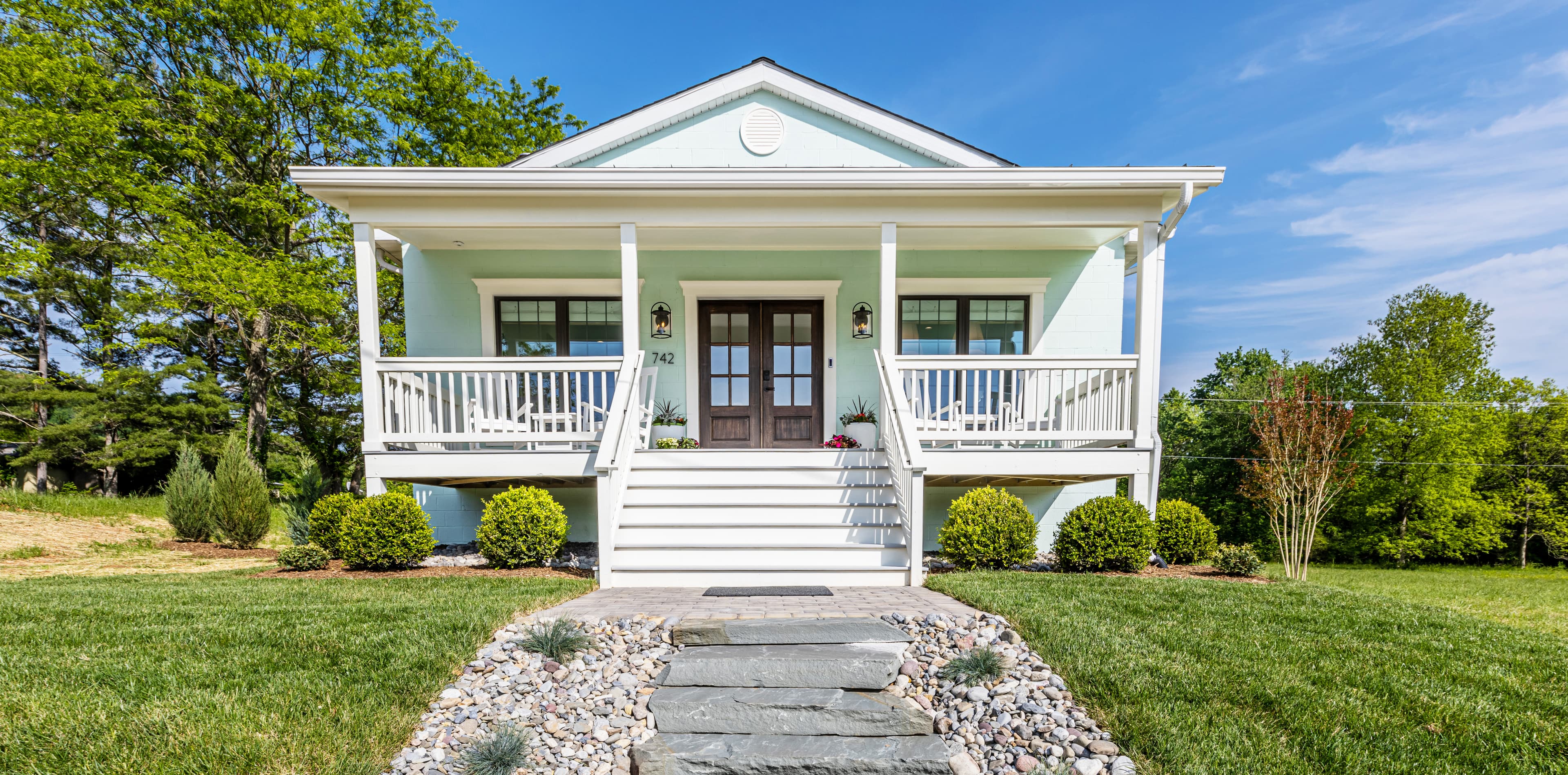 A pale blue house with a front porch, steps, and neatly landscaped yard.