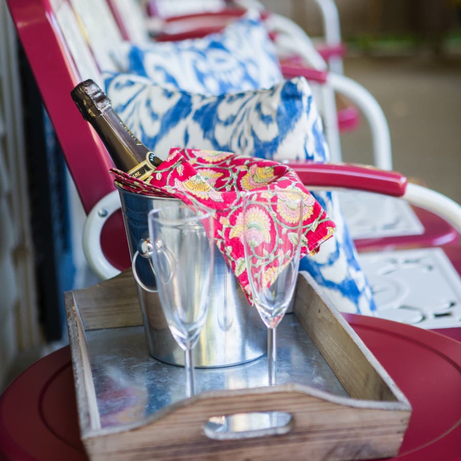 A bottle of champagne in a bucket, accompanied by two glasses and a decorative cloth on a wooden tray.